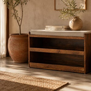 May include: A rectangular wooden shoe storage bench featuring a dark brown wood frame with two open shelves and a light beige upholstered seat cushion on top. The bench has a clean, functional design with a sturdy base and a smooth, polished finish.