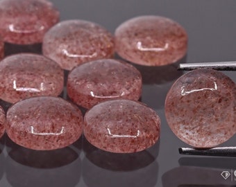 May include: A group of 10 round, translucent, pink, and red gemstone cabochons. The cabochons are smooth and have a speckled appearance. One cabochon is being held by tweezers.