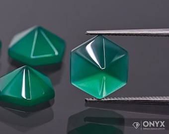 Pode incluir: Close-up de uma gema verde com forma hexagonal facetada. A gema está sendo segurada por uma pinça e está cercada por outras gemas semelhantes.
