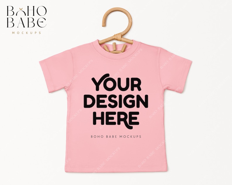 May include: Pink t-shirt mockup with a hanger. The shirt has the text "YOUR DESIGN HERE" and "BOHO BABE MOCKUPS" printed on it.
