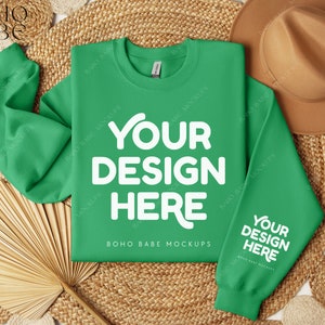 May include: A bright green sweatshirt with the text "YOUR DESIGN HERE" in white on the front and back. The sweatshirt is laid flat on a woven straw mat with a brown hat and a fan.