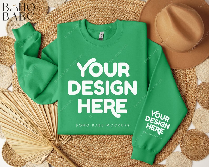 May include: A bright green sweatshirt with the text "YOUR DESIGN HERE" in white on the front and back. The sweatshirt is laid flat on a woven straw mat with a brown hat and a fan.