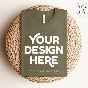 Może przedstawiać: Złożony oliwkowy t-shirt z napisem "YOUR DESIGN HERE" w kolorze białym na plecionym słomkowym dywaniku. Na koszulce nadrukowany jest napis "BOHO BABE MOCKUPS".