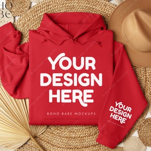 May include: Red hooded sweatshirt with the text "YOUR DESIGN HERE" on the front and back. The sweatshirt is laid out on a woven surface with a straw hat and a palm leaf fan.