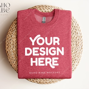 May include: A red heather t-shirt folded on a woven straw placemat. The t-shirt has the text "YOUR DESIGN HERE" printed in white on the front.