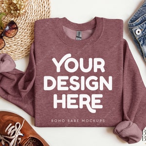 May include: A maroon sweatshirt with the text "YOUR DESIGN HERE" in white on the front. The sweatshirt is laid flat on a white surface with a pair of brown shoes, a woven straw mat, sunglasses, and a pair of denim shorts.