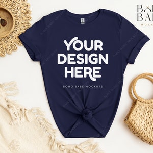 May include: A navy blue t-shirt with the text "YOUR DESIGN HERE" in white. The shirt is laid flat on a white surface with a woven basket and a white blanket.