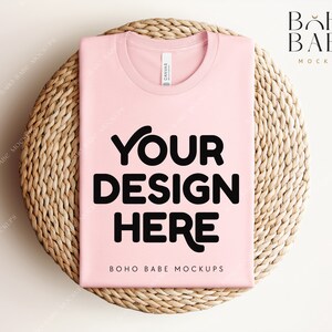 Może przedstawiać: Makieta r&oacute;żowej koszulki z nadrukiem "YOUR DESIGN HERE" na okrągłej plecionej macie. Na dole koszulki widnieje napis "BOHO BABE MOCKUPS".