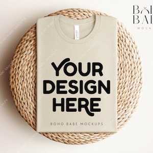 Może przedstawiać: Makieta beżowej koszulki z nadrukiem "YOUR DESIGN HERE" i "BOHO BABE MOCKUPS" na tle plecionej powierzchni z wikliny.