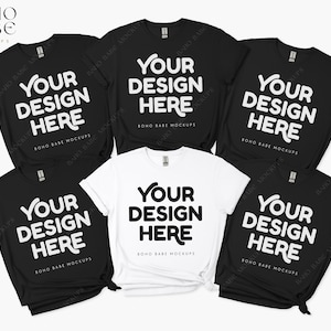 May include: Five t-shirts, two black and three white, are arranged in a pile. Each shirt has the text "Your Design Here" printed on the front in a bold, white font. The shirts are a mockup for a design project.