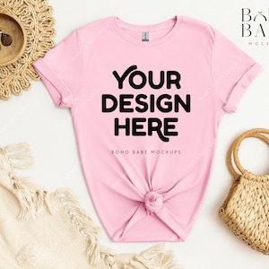 May include: Pink t-shirt mockup with the text "YOUR DESIGN HERE" and the words "BOHO BABE MOCKUPS" below. The t-shirt is laid flat on a white surface with a woven basket and a blanket.
