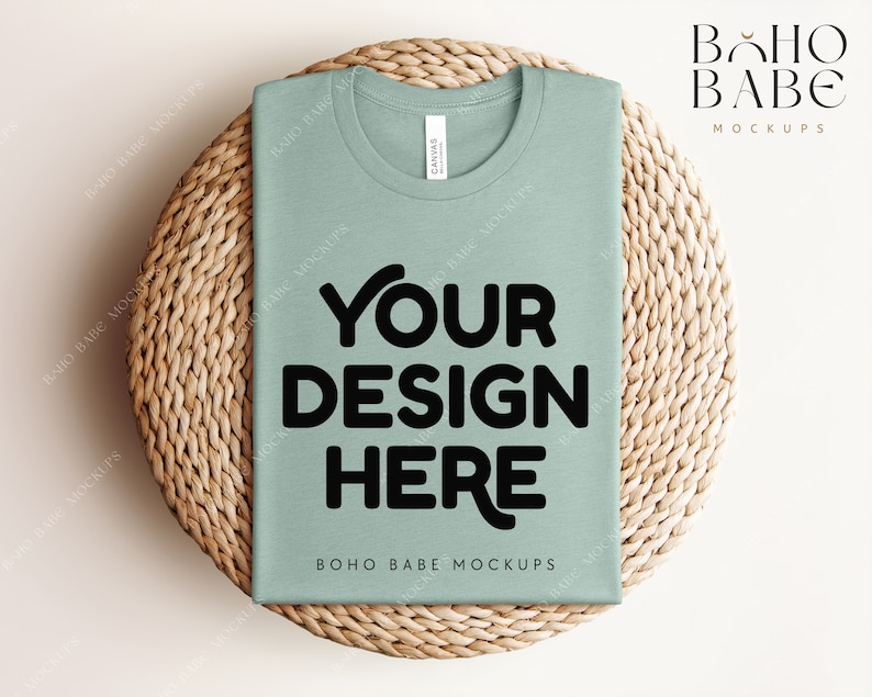 Może przedstawiać: Makieta koszulki w kolorze szałwiowej zieleni na plecionym podkładce ze słomy. Na koszulce znajduje się napis "YOUR DESIGN HERE" wydrukowany czarnym kolorem.