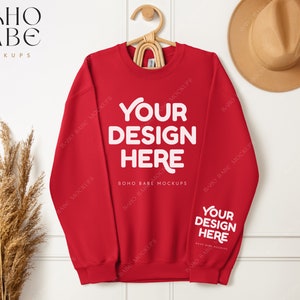 May include: Red sweatshirt mockup with the text "Your Design Here" on the front and back. The sweatshirt is hanging on a wooden hanger against a white wall.
