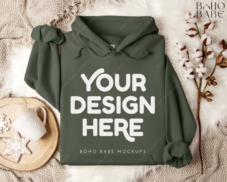 Puede incluir: Una sudadera con capucha verde con el texto "YOUR DESIGN HERE" en blanco en la parte delantera. La sudadera est&aacute; sobre una superficie blanca y peluda con una bandeja de madera y una taza blanca con un dise&ntilde;o de coraz&oacute;n.