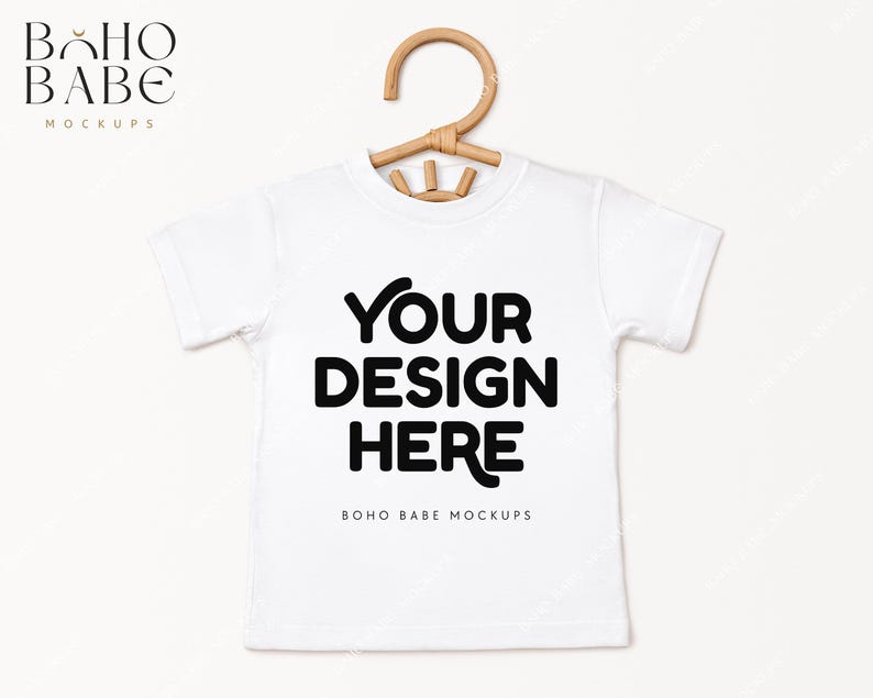 May include: White t-shirt mockup with a wooden hanger. The shirt has the text "YOUR DESIGN HERE" and "BOHO BABE MOCKUPS" printed on it.