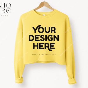 Peut inclure: Sweat-shirt jaune à manches longues et coupe courte. Le sweat-shirt porte l'inscription "YOUR DESIGN HERE" sur le devant.