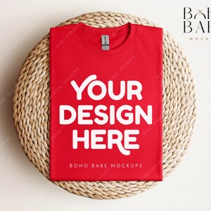 May include: Red t-shirt mockup on a woven straw mat. The t-shirt has the text "YOUR DESIGN HERE" in white. The text "BOHO BABE MOCKUPS" is also visible on the t-shirt.