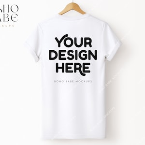 May include: White t-shirt mockup with the text "YOUR DESIGN HERE" printed on the back. The shirt is hanging on a wooden hanger against a white background.