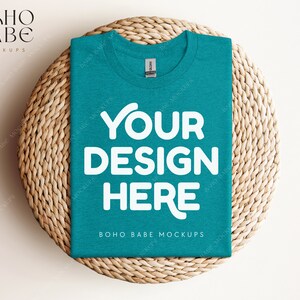 May include: A teal blue t-shirt with the text "YOUR DESIGN HERE" in white on a woven straw mat.  BOHO BABE MOCKUPS is printed on the bottom of the shirt.
