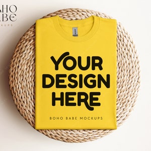 Puede incluir: Maqueta de camiseta amarilla sobre un mantel individual de paja trenzada. La camiseta tiene el texto "YOUR DESIGN HERE" y "BOHO BABE MOCKUPS" impreso en ella.
