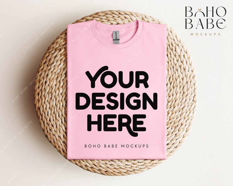 Op de afbeelding: Een roze t-shirt mockup met de tekst "YOUR DESIGN HERE" op een geweven stro mat. De tekst "BOHO BABE MOCKUPS" staat onderaan het shirt.