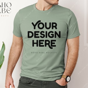 May include: A sage green t-shirt with short sleeves and a crew neck. The shirt has the text "YOUR DESIGN HERE" printed on the front in black.