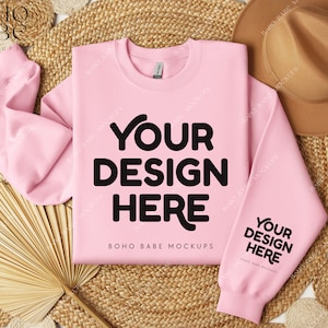 Puede incluir: Una maqueta de sudadera rosa con el texto "Your Design Here" y "BOHO BABE MOCKUPS" sobre un fondo tejido natural con un sombrero de paja y un abanico.