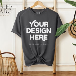 May include: A dark gray t-shirt mockup with the text "YOUR DESIGN HERE" and "BOHO BABE MOCKUPS" on a wooden hanger against a white wall.