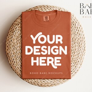May include: A rust-colored t-shirt mockup with the text "YOUR DESIGN HERE" in white on a woven straw mat. The text "BOHO BABE MOCKUPS" is also visible on the t-shirt.