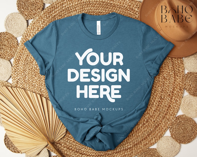 Peut inclure: Un t-shirt bleu sarcelle avec le texte "YOUR DESIGN HERE" en blanc, pr&eacute;sent&eacute; sur un tapis tiss&eacute; avec des &eacute;l&eacute;ments d&eacute;coratifs. Le t-shirt est une maquette, parfaite pour pr&eacute;senter des cr&eacute;ations.