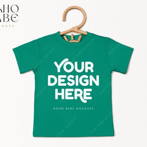 May include: A green t-shirt mockup with a hanger. The shirt has the text "YOUR DESIGN HERE" and "BOHO BABE MOCKUPS" printed on it.