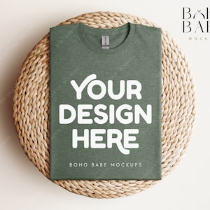 Op de afbeelding: Een groene t-shirt mockup op een geweven strooien placemat. Het t-shirt heeft de tekst "YOUR DESIGN HERE" en "BOHO BABE MOCKUPS" erop gedrukt.