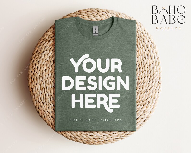 Op de afbeelding: Een groene t-shirt mockup op een geweven strooien placemat. Het t-shirt heeft de tekst "YOUR DESIGN HERE" en "BOHO BABE MOCKUPS" erop gedrukt.