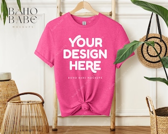 May include: Pink t-shirt mockup with the text "YOUR DESIGN HERE" on a hanger against a white wall with a wooden ladder and a wicker basket.