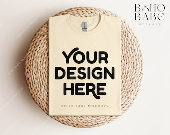 May include: A beige t-shirt mockup on a woven round mat. The t-shirt has the text "YOUR DESIGN HERE" printed in black.