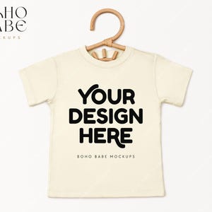 May include: A white t-shirt mockup with a wooden hanger. The text "YOUR DESIGN HERE" is printed on the front of the shirt. The text "BOHO BABE MOCKUPS" is printed below the design.