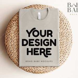 Puede incluir: Una camiseta gris claro con el texto "YOUR DESIGN HERE" en negro sobre una superficie de mimbre tejido. El texto "BOHO BABE MOCKUPS" también es visible en la camiseta.