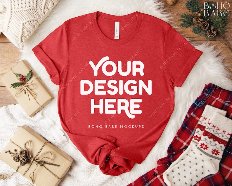 May include: A red t-shirt with the text "YOUR DESIGN HERE" in white, displayed on a white fur-like surface. The shirt is accompanied by wrapped gifts, a pair of plaid pajama pants, and a pair of patterned socks. The scene is set on a wooden surface.