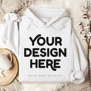 Puede incluir: Maqueta de sudadera con capucha blanca con el texto "YOUR DESIGN HERE" y "BOHO BABE MOCKUPS" sobre un fondo de piel sint&eacute;tica blanca con una bandeja de madera y una taza.