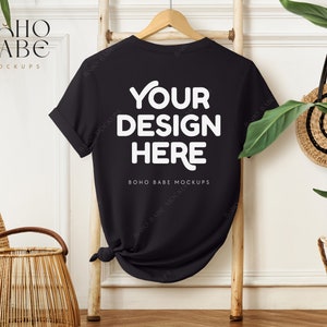 Könnte beinhalten: Schwarzes T-Shirt-Mockup mit dem Text "YOUR DESIGN HERE" und "BOHO BABE MOCKUPS" auf einer Holzleiter mit einem Weidenkorb und einem geflochtenen Hut im Hintergrund.