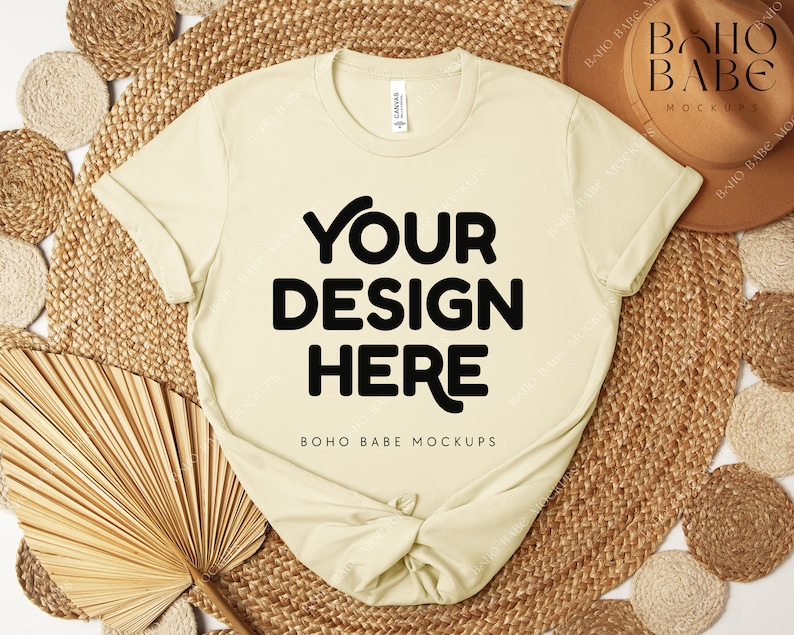 Peut inclure: Un t-shirt cr&egrave;me avec le texte "YOUR DESIGN HERE" en lettres noires en gras. Le t-shirt est pr&eacute;sent&eacute; sur un tapis tiss&eacute; avec un chapeau marron et des &eacute;l&eacute;ments d&eacute;coratifs. Les mots "BOHO BABE MOCKUPS" sont &eacute;galement visibles.