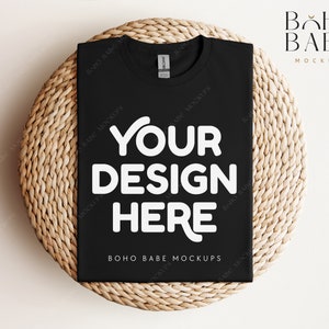 Könnte beinhalten: Ein schwarzes T-Shirt mit dem weißen Text "YOUR DESIGN HERE", präsentiert auf einer gewebten, kreisförmigen Oberfläche. Das Shirt ist von der Marke Gildan. Die Worte "BOHO BABE MOCKUPS" sind ebenfalls sichtbar.