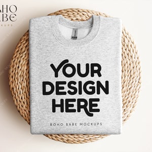 以下が含まれることがあります： 織り籐の表面に「YOUR DESIGN HERE」と「BOHO BABE MOCKUPS」のテキストが書かれたグレーのトレーナーのモックアップです。
