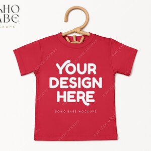 May include: Red short-sleeved t-shirt with the text "YOUR DESIGN HERE" and "BOHO BABE MOCKUPS" printed on the front.