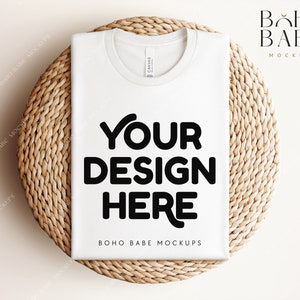 Może przedstawiać: Biała koszulka mockupowa na okrągłej plecionej macie z tekstem "YOUR DESIGN HERE" i "BOHO BABE MOCKUPS" nadrukowanym na koszulce.
