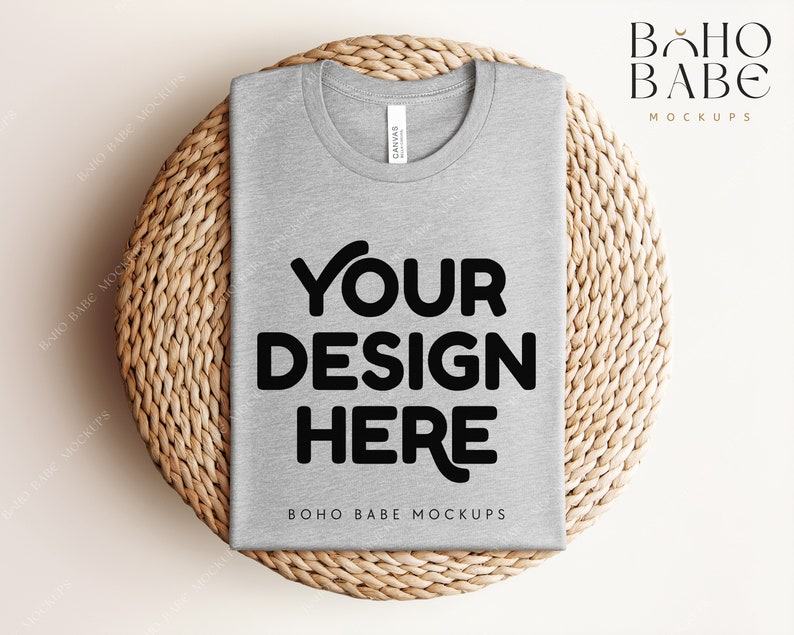 Może przedstawiać: Makieta szarego t-shirtu z nadrukiem "YOUR DESIGN HERE" na tle z plecionego wikliny.  BOHO BABE MOCKUPS jest nadrukowane na koszulce.