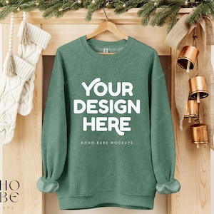 May include: A green sweatshirt with the text "YOUR DESIGN HERE" and "BOHO BABE MOCKUPS" on a wooden mantel with a garland of greenery and bells.