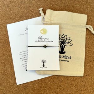 Può includere: Un braccialetto di corda nero con un piccolo perno nero. Il braccialetto è confezionato in una piccola borsa di cordoncino bianco con un disegno di fiore di loto bianco e nero. La carta recita "Manipura Solar Plexus Chakra" e "Saya Mart".