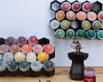 May include: Two black hexagonal paint pot organizers with rows of small paint pots. The organizers are filled with various colors of paint. A miniature figure of a warrior is standing on a black base.