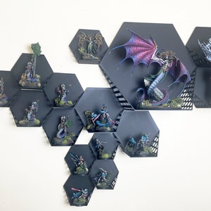 Puede incluir: Una colección de figuras en miniatura pintadas expuestas en estantes hexagonales negros. Las figuras están dispuestas en una variedad de poses e incluyen un dragón, un árbol y varias figuras humanoides.